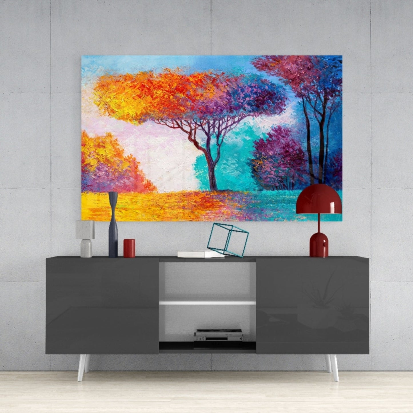 Colorful glass wall art featuring vibrant trees in yellow, orange, purple and teal displayed above a gray media console in a modern interior.