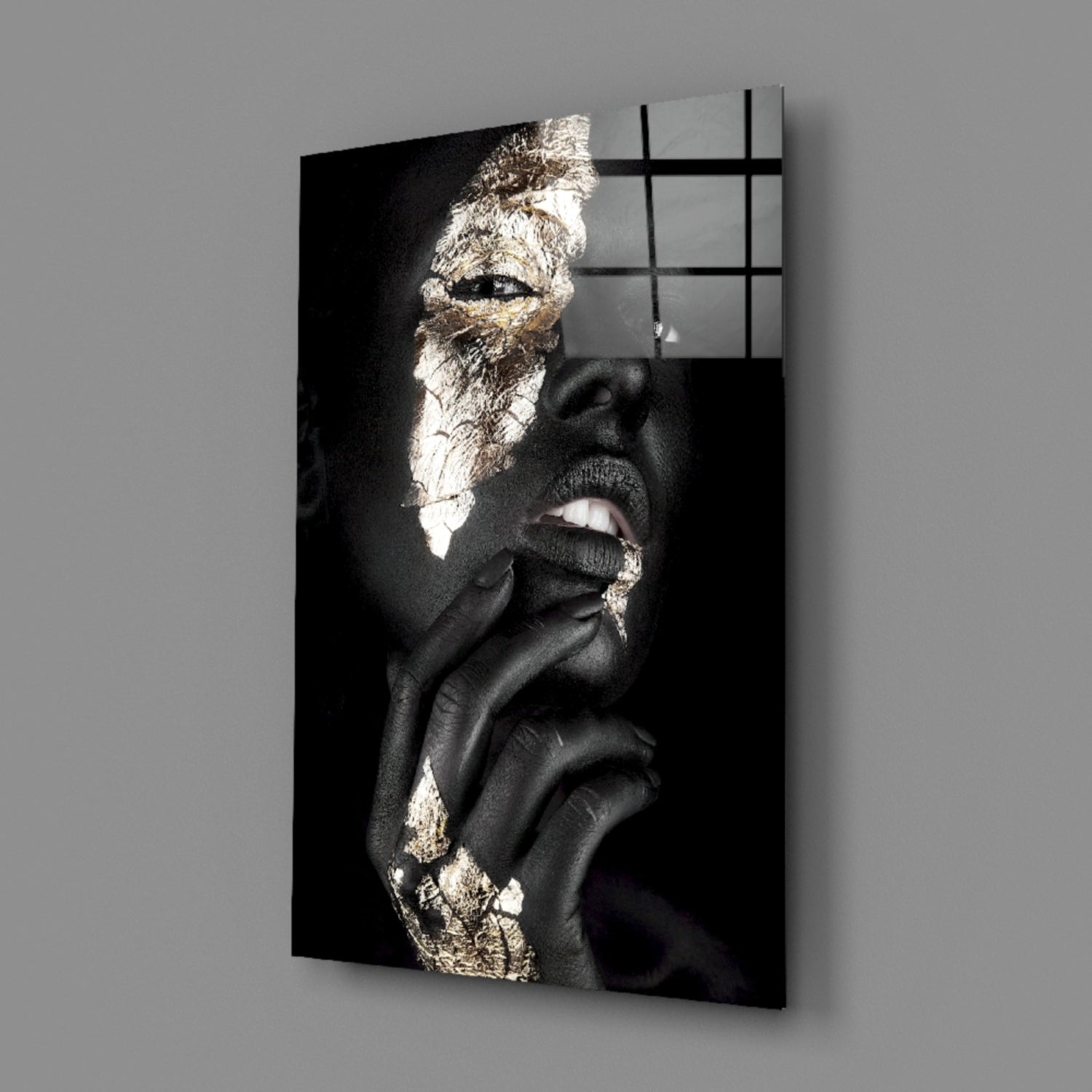 Black and gold portrait of a person with gold leaf accents on face and chest, mounted on glass wall art panel.