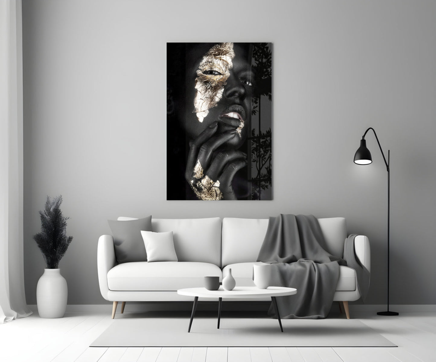 Glass wall art displaying black and white portrait of woman with gold leaf accents, hung above white sofa in minimalist interior.