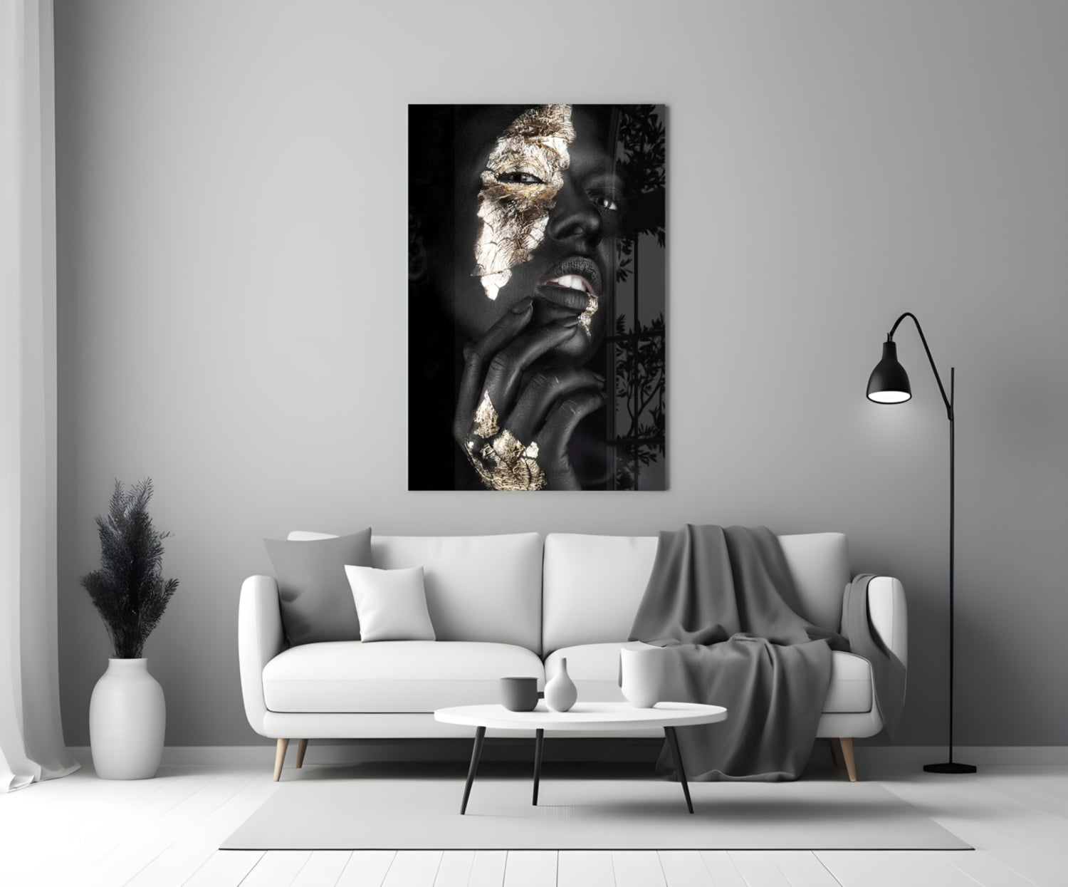 Glass wall art displaying black and white portrait of woman with gold leaf accents, hung above white sofa in minimalist interior.