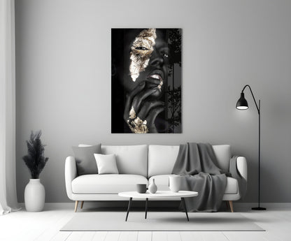 Glass wall art displaying black and white portrait of woman with gold leaf accents, hung above white sofa in minimalist interior.