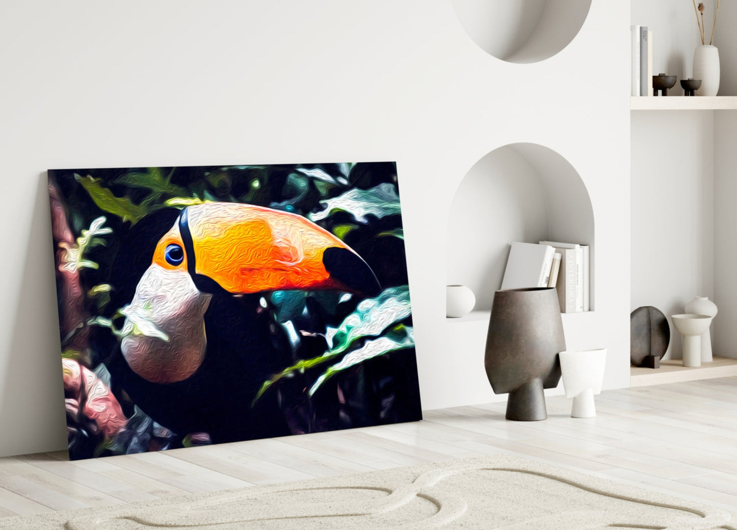 Toco Toucan glass wall art leaning against white wall in minimalist room with sand floor and decorative objects.
