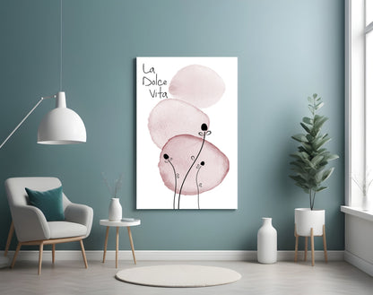 La Dolce Vita glass wall art displaying pink watercolor circles with thin black line stems, hung in a teal room with white furniture and plants.