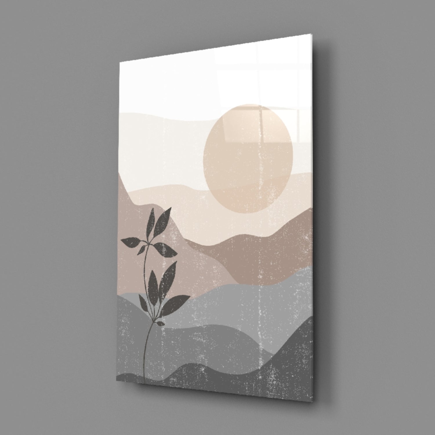 Angled perspective view of glass wall art displaying layered landscape with beige and gray tones, botanical stem, and circular moon against white background.