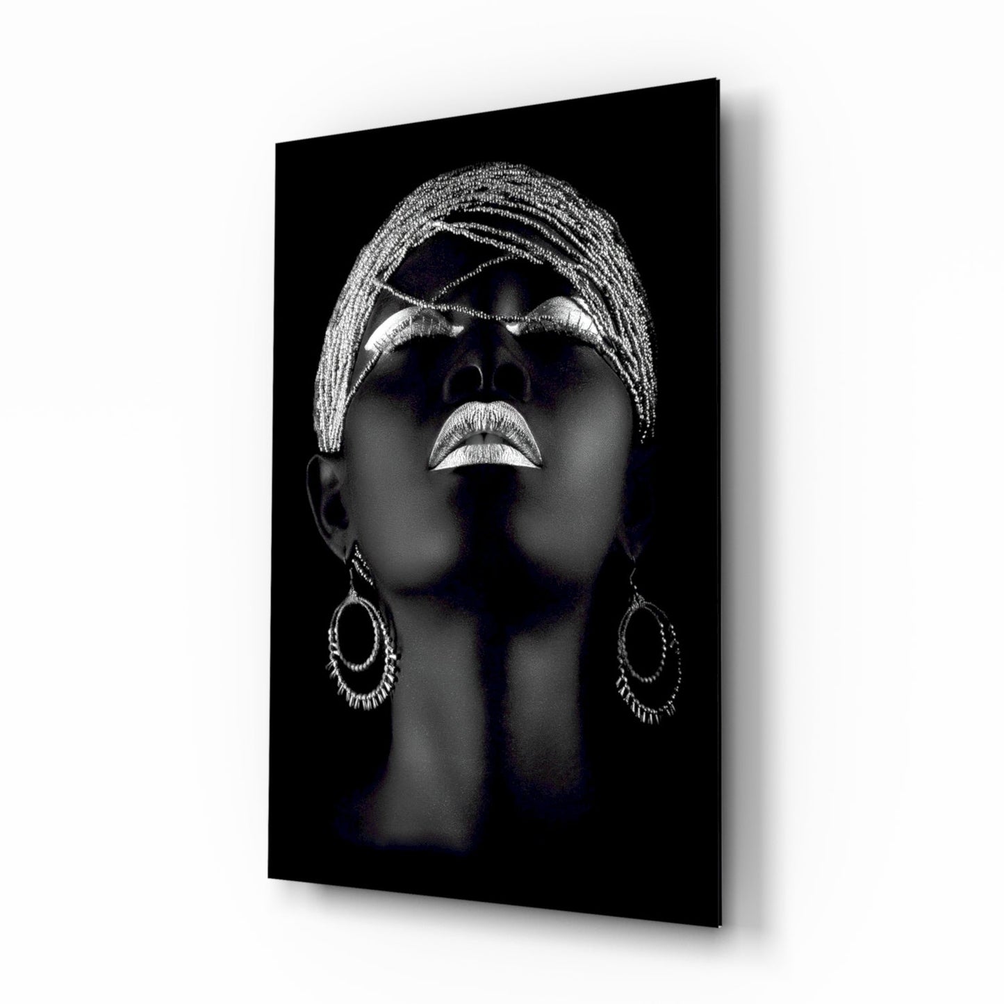 Black glass wall art featuring a silver-highlighted portrait of a woman's face tilted upward, wearing ornate hoop earrings and braided head wrap.