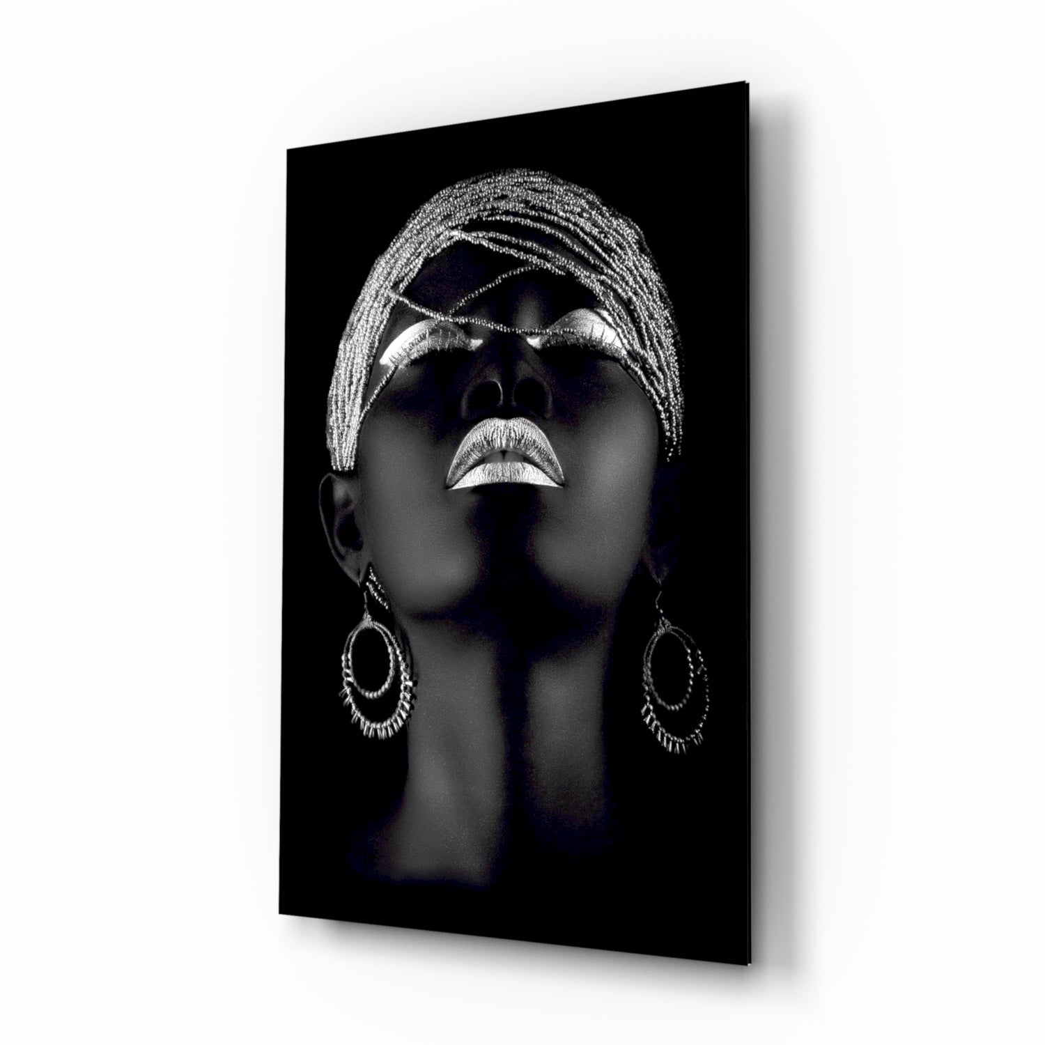 Black glass wall art featuring a silver-highlighted portrait of a woman's face tilted upward, wearing ornate hoop earrings and braided head wrap.