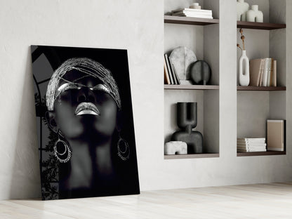 Black and white glass portrait of woman wearing sunglasses and hoop earrings, leaning against white wall with wooden shelves.