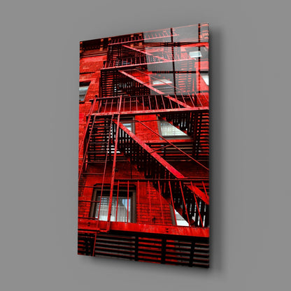 Red brick building facade with black metal fire escape stairs and windows displayed on glass wall art panel against gray background.