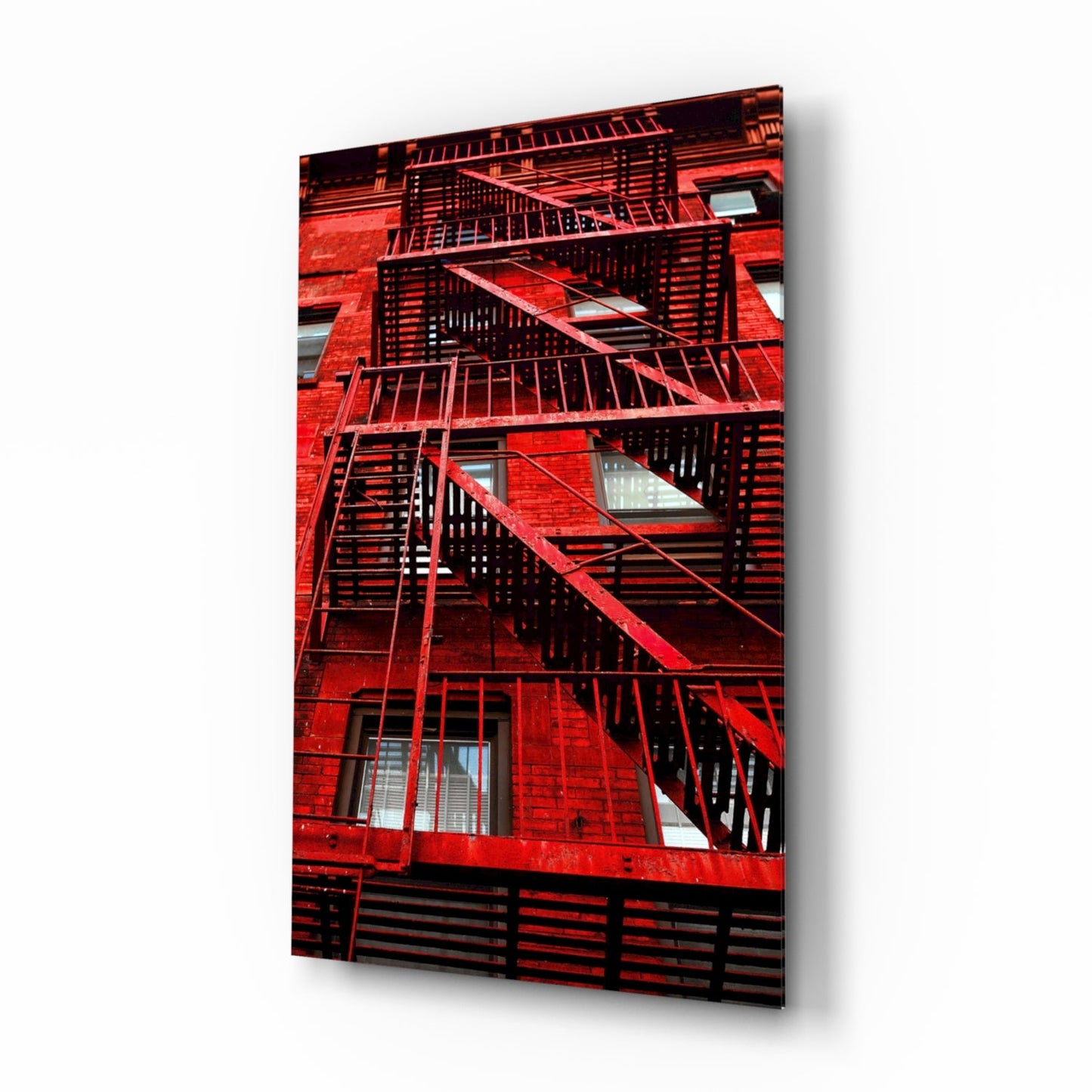 Red painted brick building facade with black metal fire escape stairs and railings, with windows visible between landings.