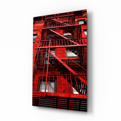 Red painted brick building facade with black metal fire escape stairs and railings, with windows visible between landings.
