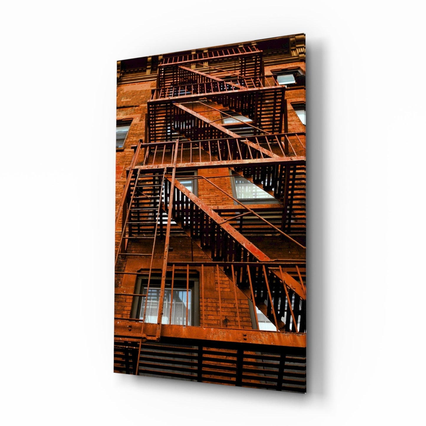 Rusty metal fire escape stairs zigzagging down a brick building facade with windows.