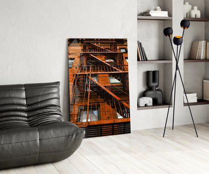 Orange Stairs glass wall art displayed in modern living room with gray leather chair, black floor lamp, and white shelving unit.
