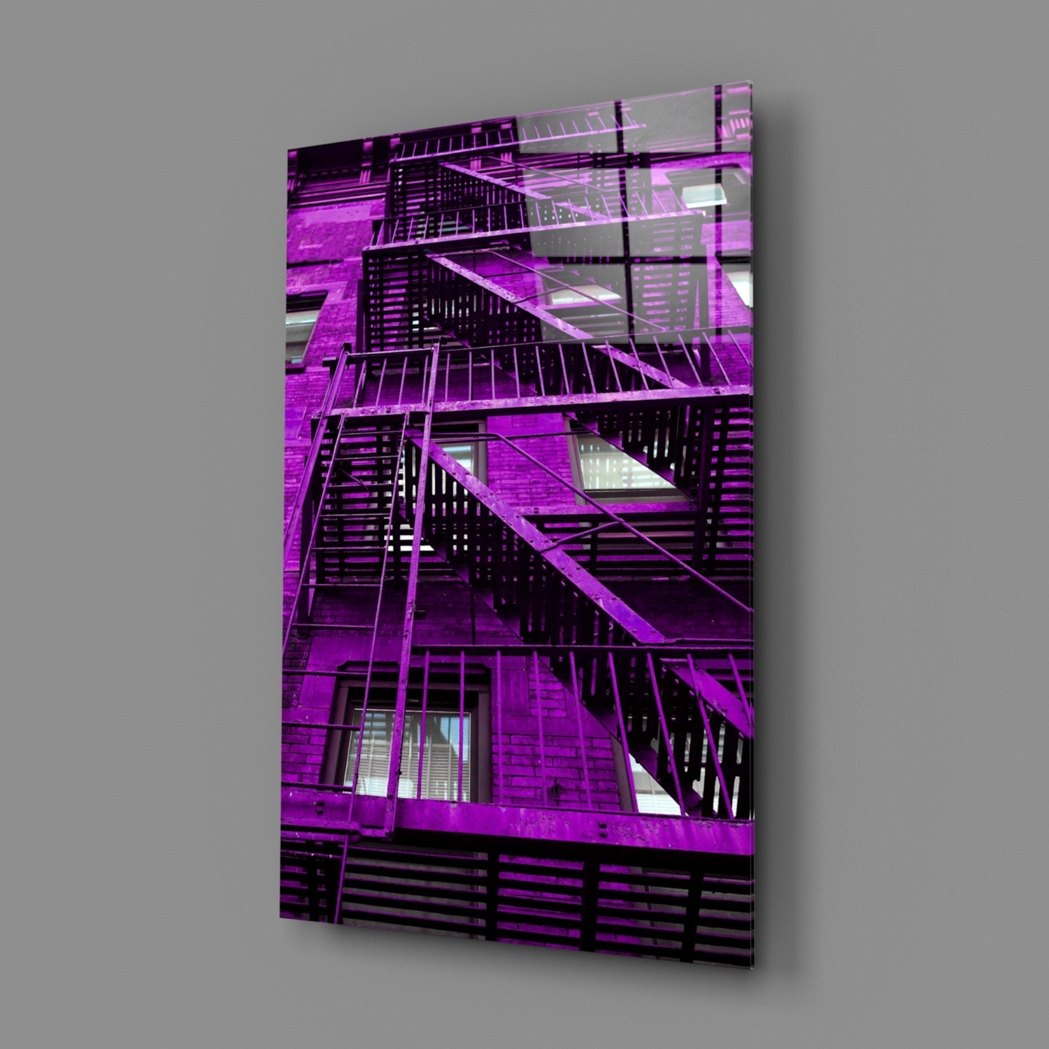 Mounted glass wall art displaying a vibrant purple-lit building facade with external fire escape stairs and windows against gray background.