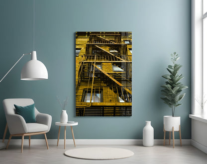 Yellow metal fire escape stairs on building facade displayed as glass wall art in modern teal interior setting.
