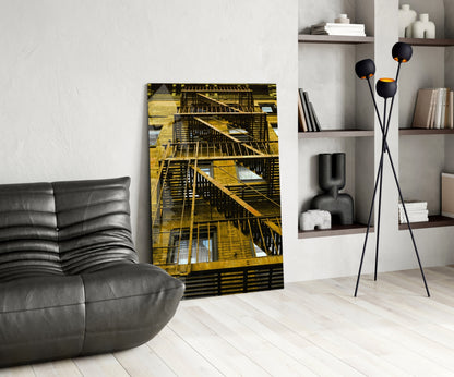 Yellow metal fire escape stairs on a building displayed as glass wall art in a modern living room with black furniture and shelving.
