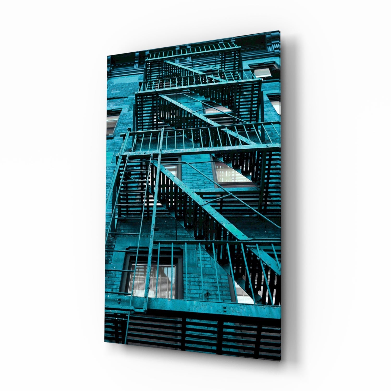 Turquoise metal fire escape stairs on brick building facade mounted as glass wall art display.