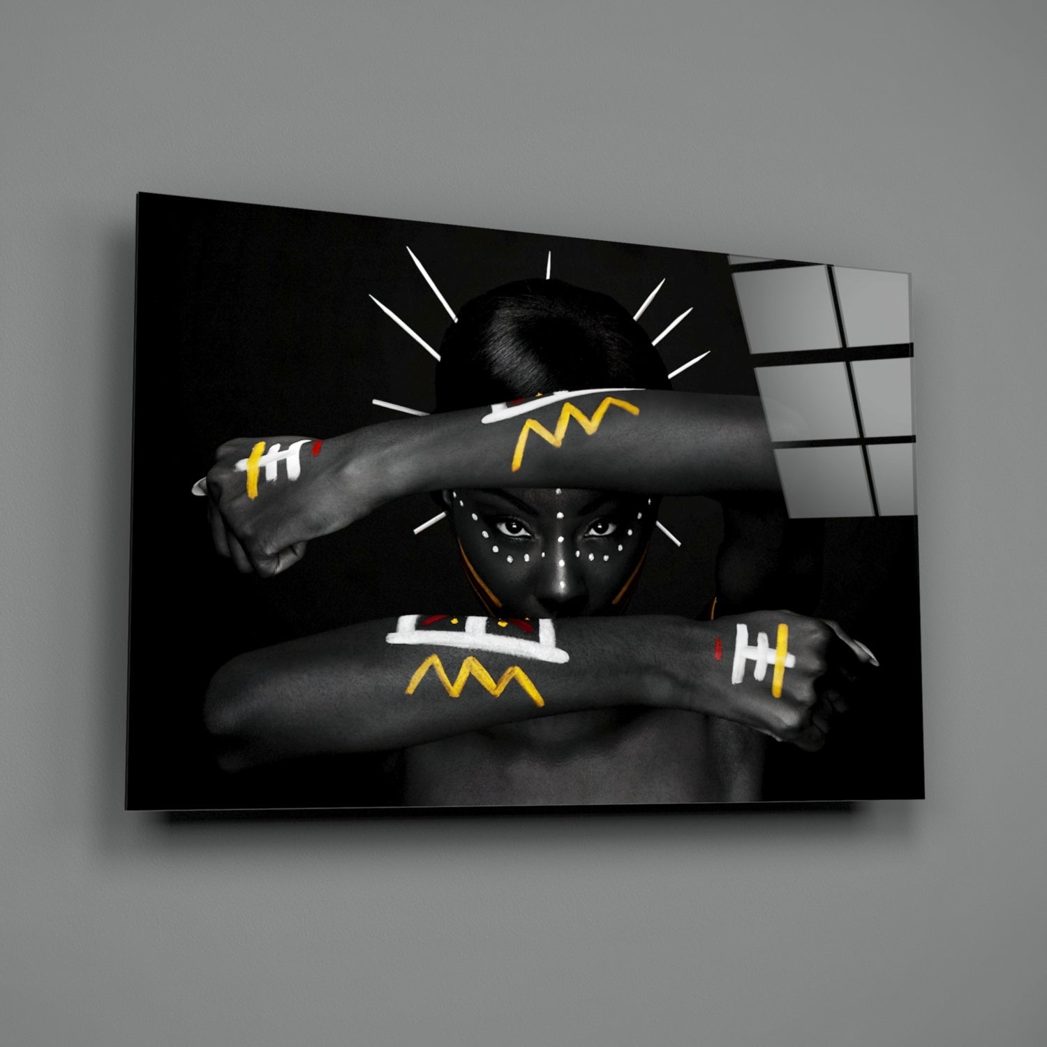 Black and white glass wall art depicting a figure with face paint and yellow geometric arm designs against dark background with white radiating lines.