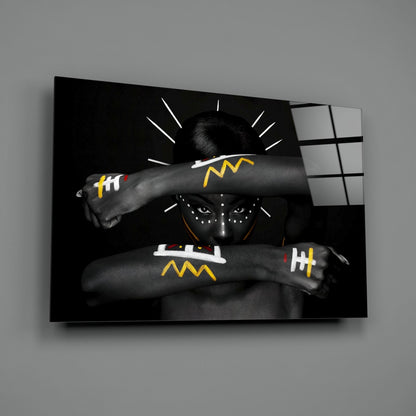 Black and white glass wall art depicting a figure with face paint and yellow geometric arm designs against dark background with white radiating lines.