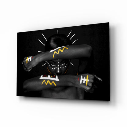 Black and white portrait of figure with decorative face paint wearing beaded necklace and patterned arm wraps with yellow and white geometric designs.