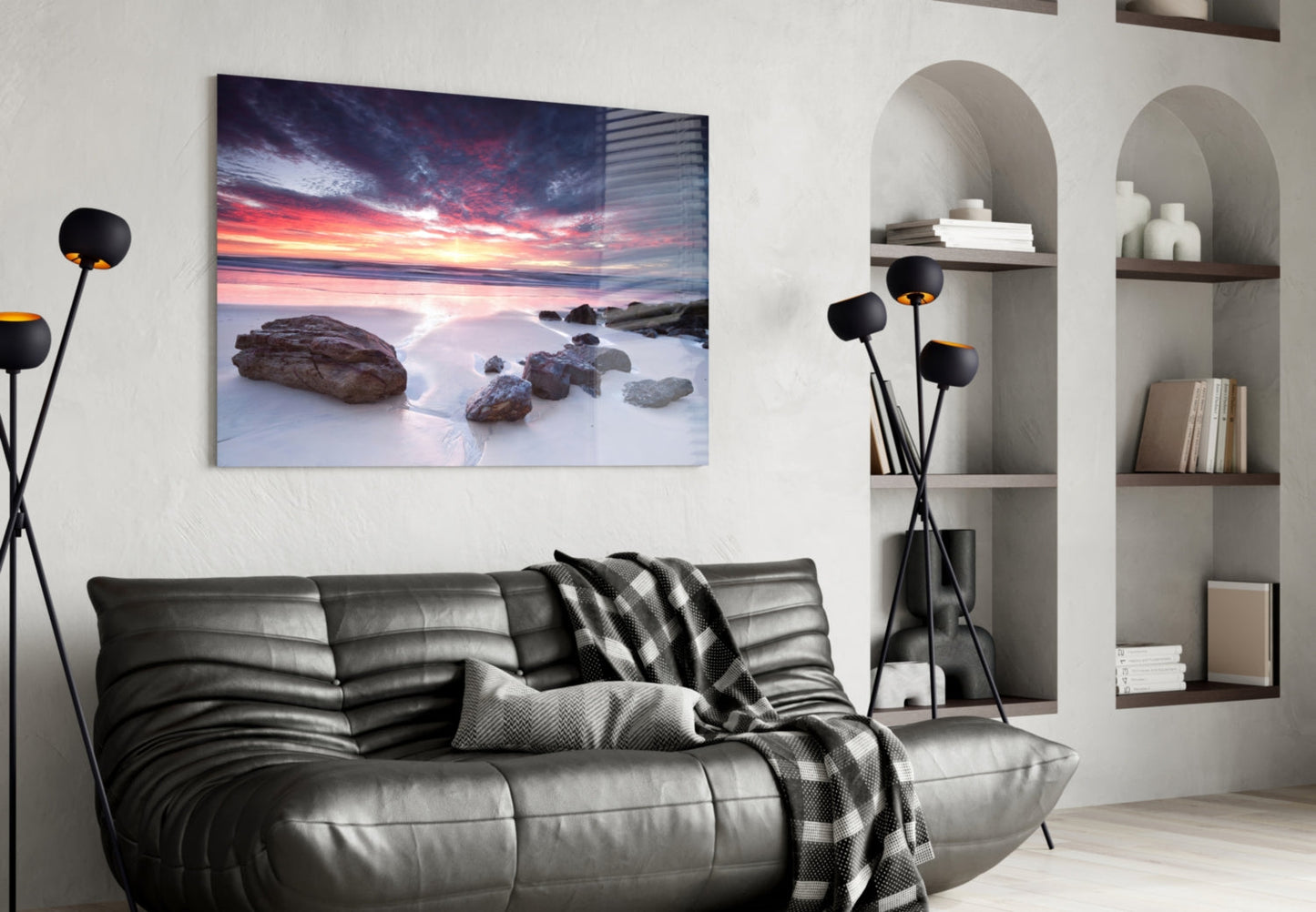Sunset beach landscape glass wall art hanging above black leather sofa in modern living room interior.