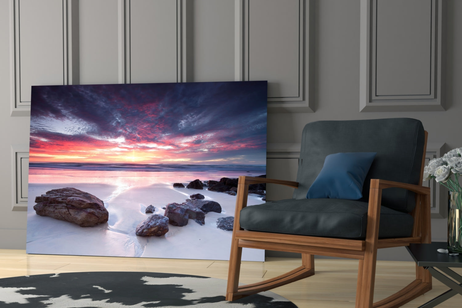 Glass wall art displaying a dramatic sunset beach scene with golden and pink clouds reflected in wet sand and rocky formations.