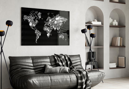 Black and white world map glass wall art displayed above a gray leather sofa in a modern living room setting.