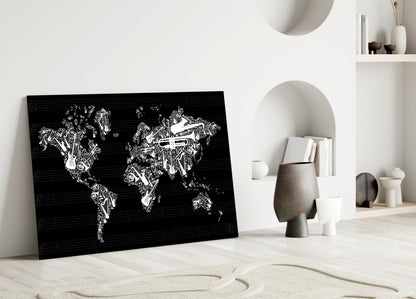 Black glass wall art featuring white musical instruments forming a world map, leaning against white wall in minimalist interior setting.