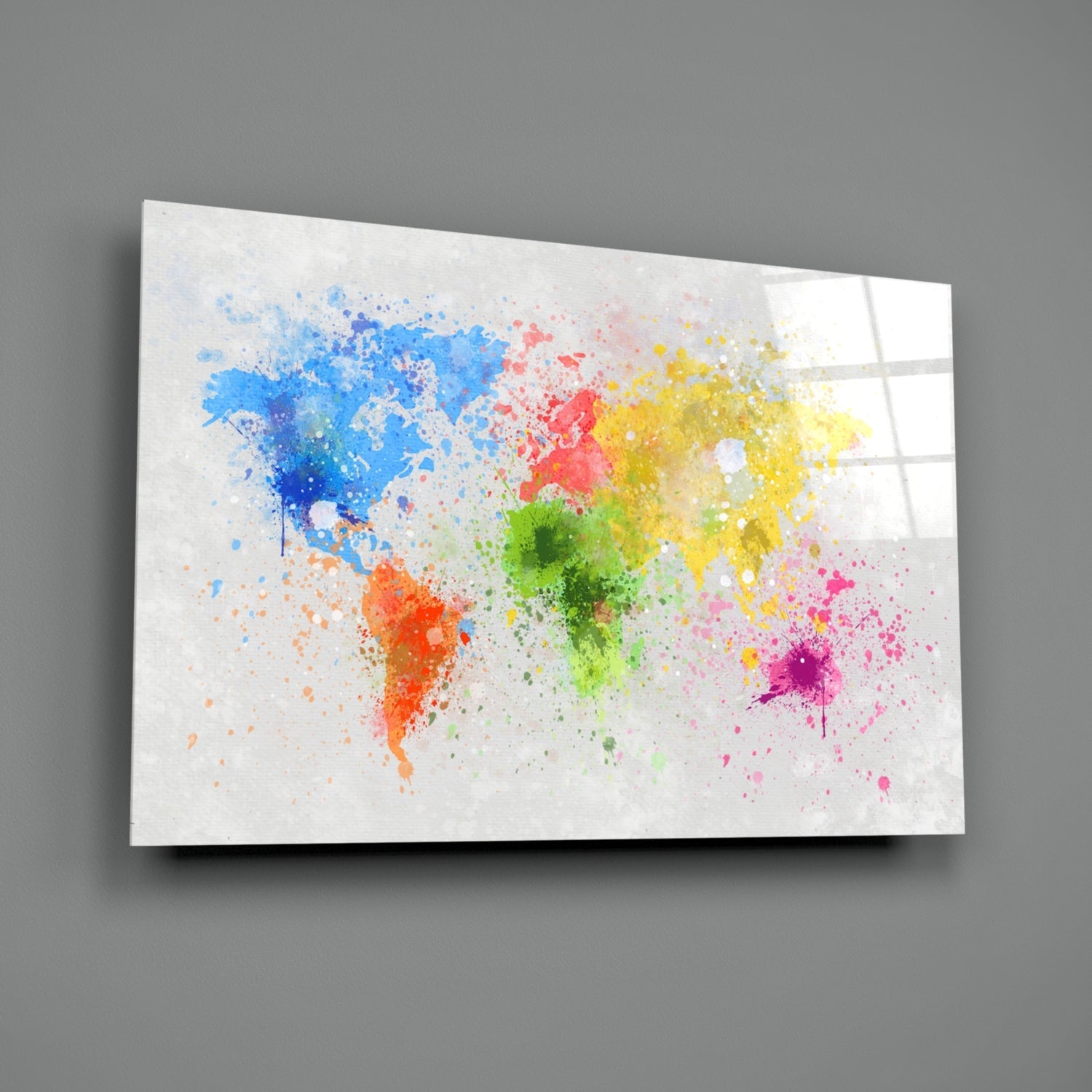 Colorful watercolor world map splashes on white glass panel displayed at angle against gray wall.