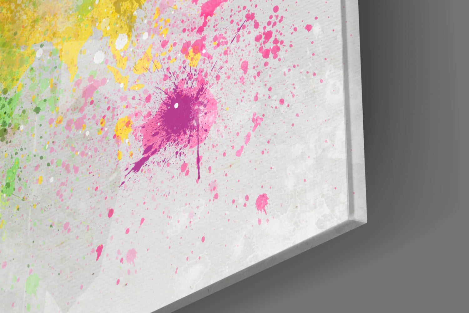 Close-up angled view of glass wall art with vibrant pink, yellow, and green paint splatters on white surface.