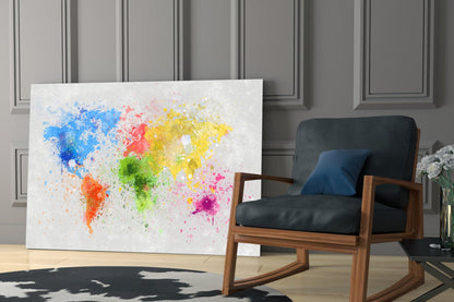 Colorful splatter world map glass wall art displayed in modern room beside wooden chair with black cushions.