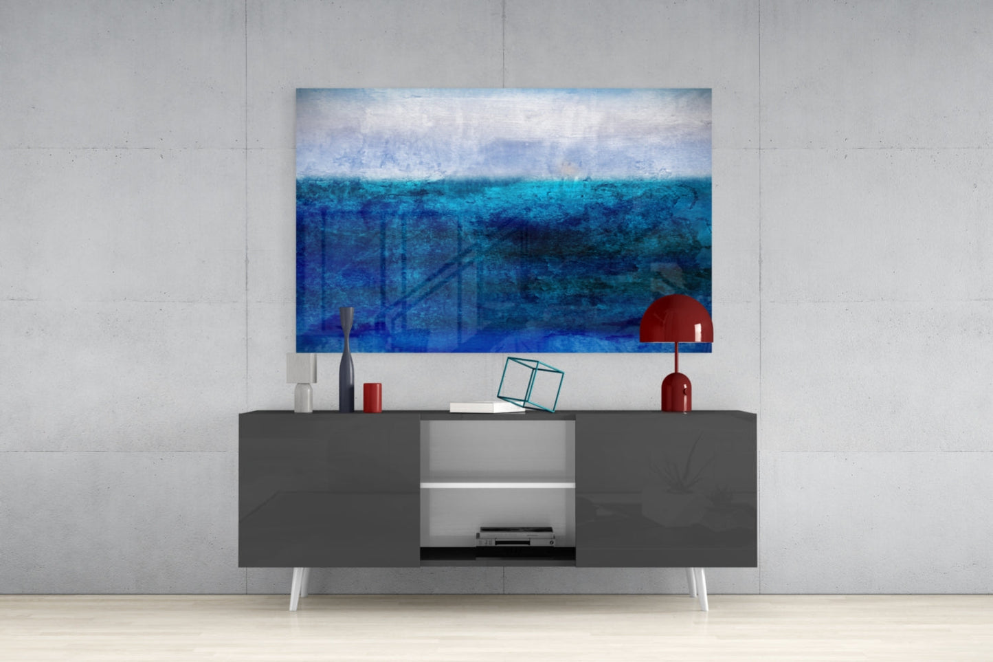 Modern living room setup featuring a blue ocean gradient glass wall art hanging above a dark gray media console with white legs and red decorative accessories.