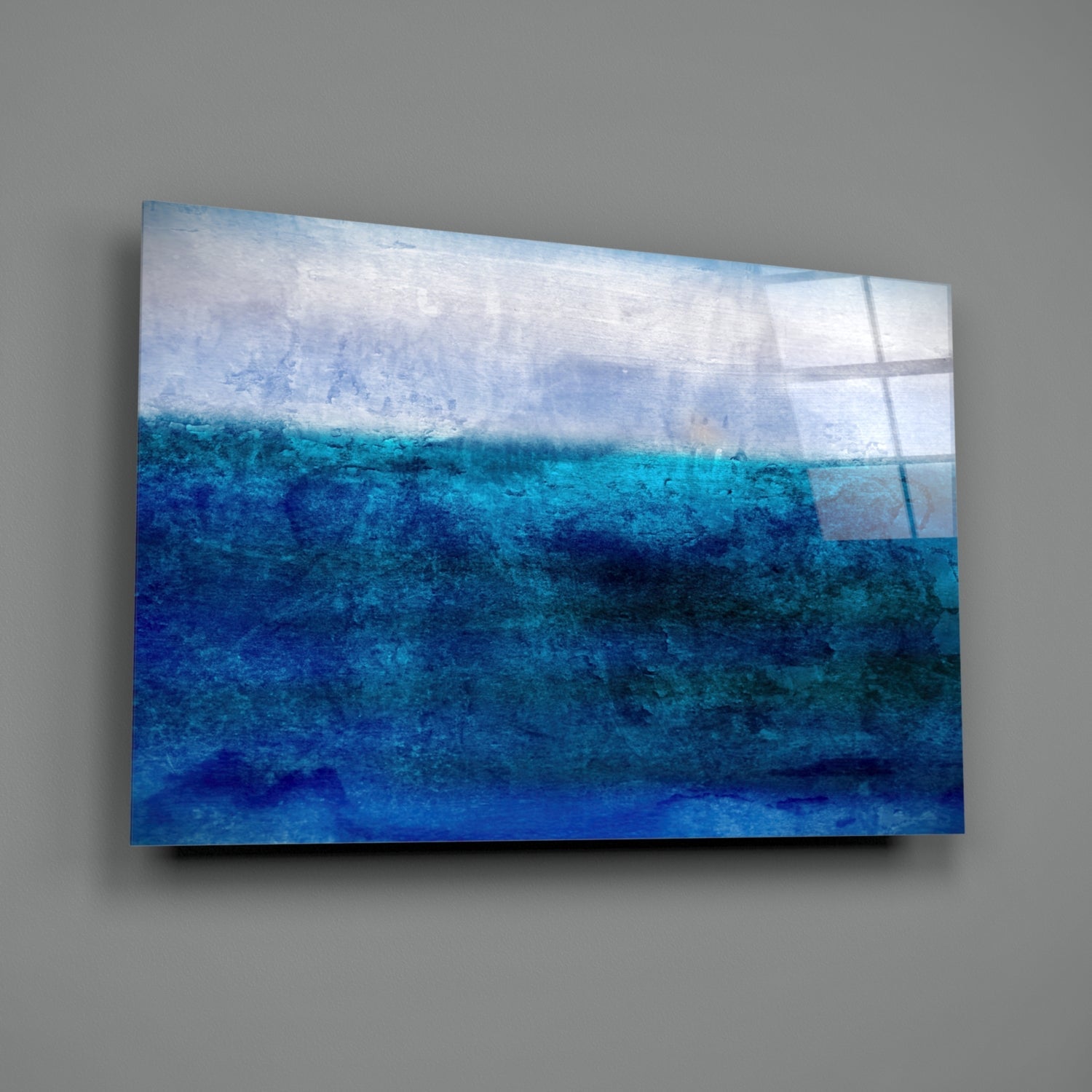 Mounted glass wall art depicting horizontal layers of white sky and graduated shades of blue ocean water with textured surface.