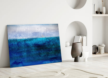 Blue gradient glass wall art leaning against white wall in minimalist interior with decorative objects and shelving.