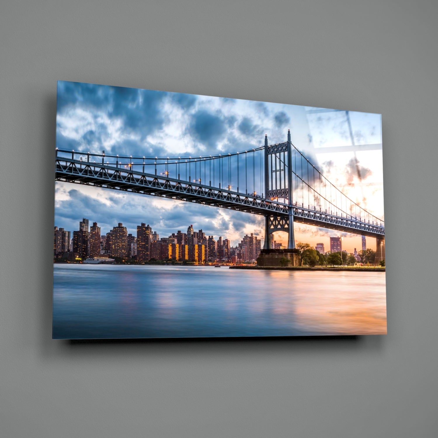 Horizontal glass wall art featuring the Queensboro Bridge spanning the East River at sunset, with Manhattan skyline and clouds reflected in the water below.