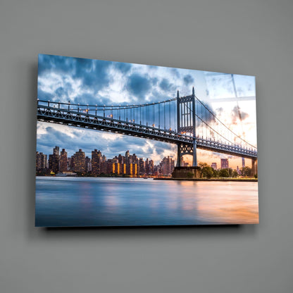 Horizontal glass wall art featuring the Queensboro Bridge spanning the East River at sunset, with Manhattan skyline and clouds reflected in the water below.