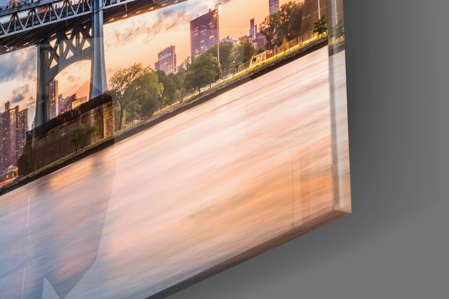 Angled view of glass wall art displaying a sunset cityscape with bridge, buildings, and waterfront, casting warm reflections on gray wall.