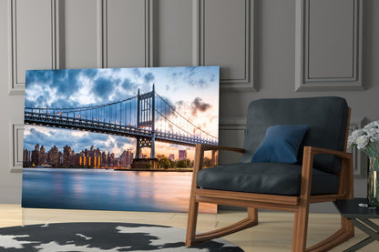 Glass wall art displaying Queensboro Bridge at sunset with Manhattan skyline, installed in modern living room beside wooden chair.