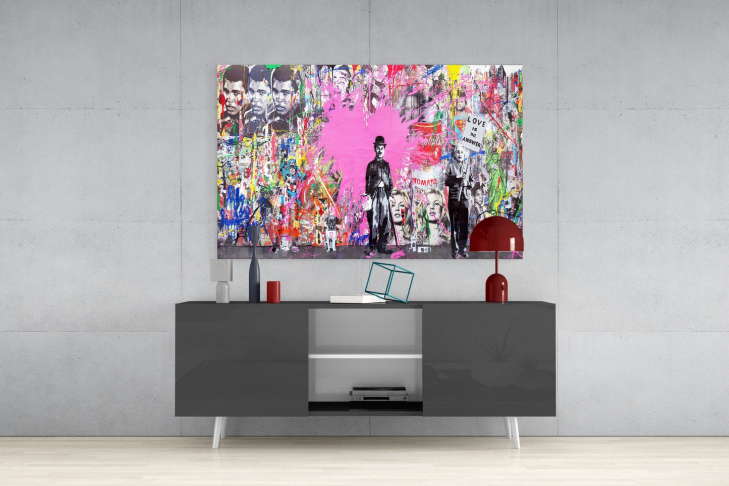 Colorful pop art glass wall art featuring black and white figures with bright pink background displayed above dark media console in modern interior.