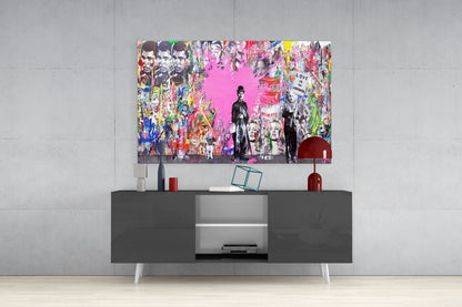 Colorful pop art glass wall art featuring black and white figures with bright pink background displayed above dark media console in modern interior.