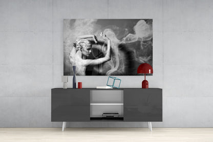 Black and white glass wall art depicting a classical figure with flowing smoke effects, displayed above a dark media console with red decorative accessories.