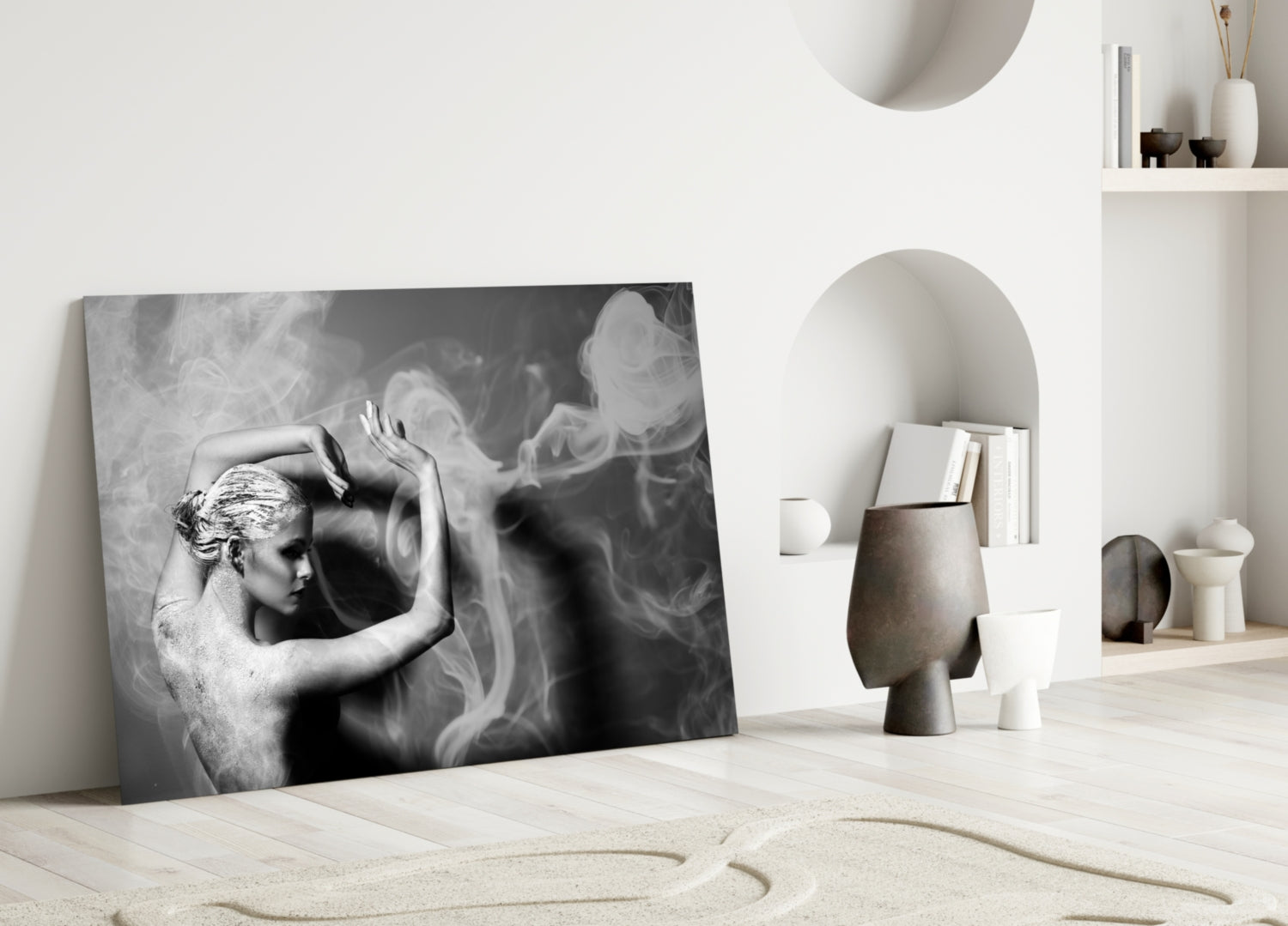 Black and white glass wall art leaning against white wall in minimalist interior with sculptural ceramics and shelving.