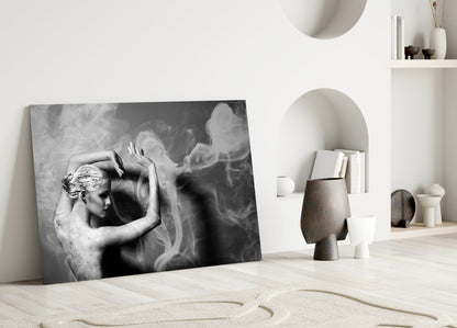 Black and white glass wall art leaning against white wall in minimalist interior with sculptural ceramics and shelving.
