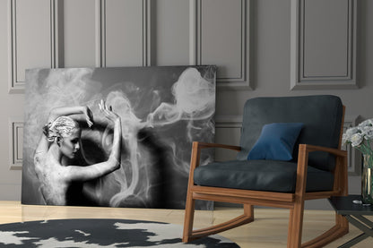 Black and white glass wall art depicting a woman's profile with flowing smoke effects, displayed in a modern living room setting beside a wooden chair.