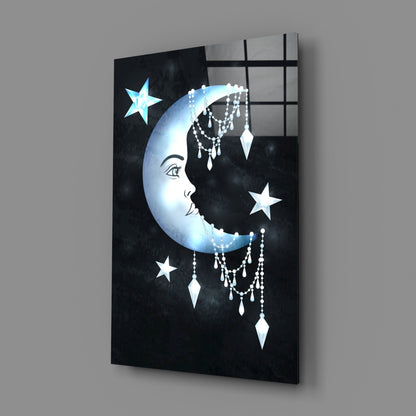 Angled view of black glass wall art featuring a luminous crescent moon with facial profile, dangling crystal beads, white stars, and grid pattern overlay.
