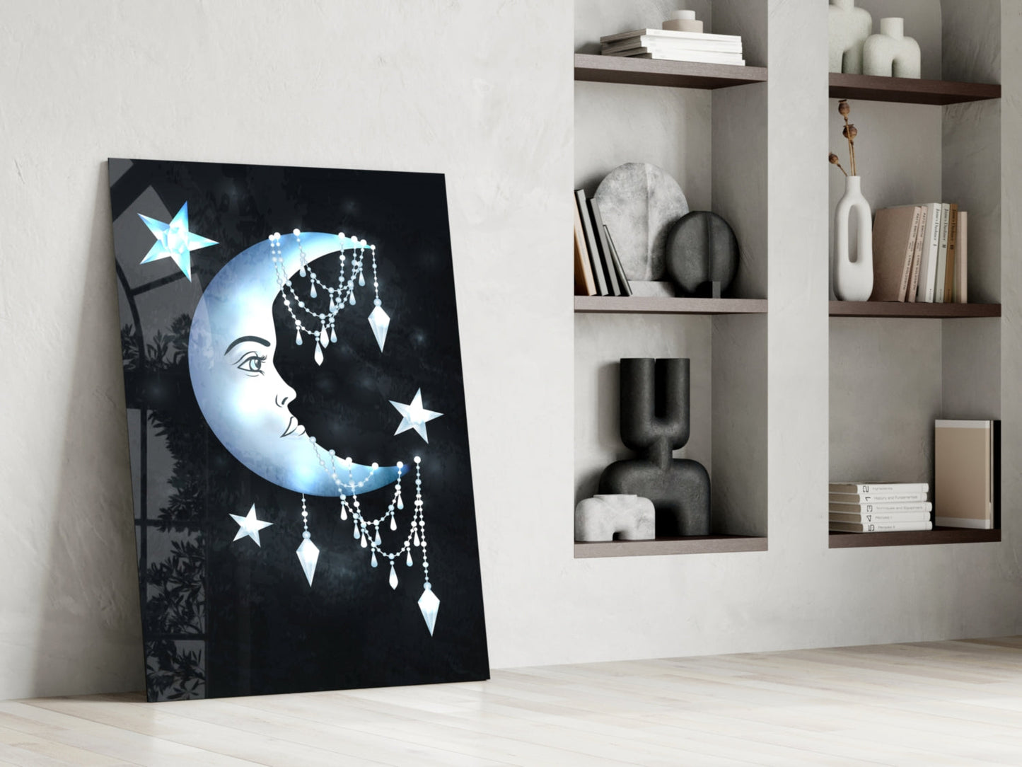 Glass wall art leaning against white wall displays blue moon face with stars and dangling crystal details beside open shelving.