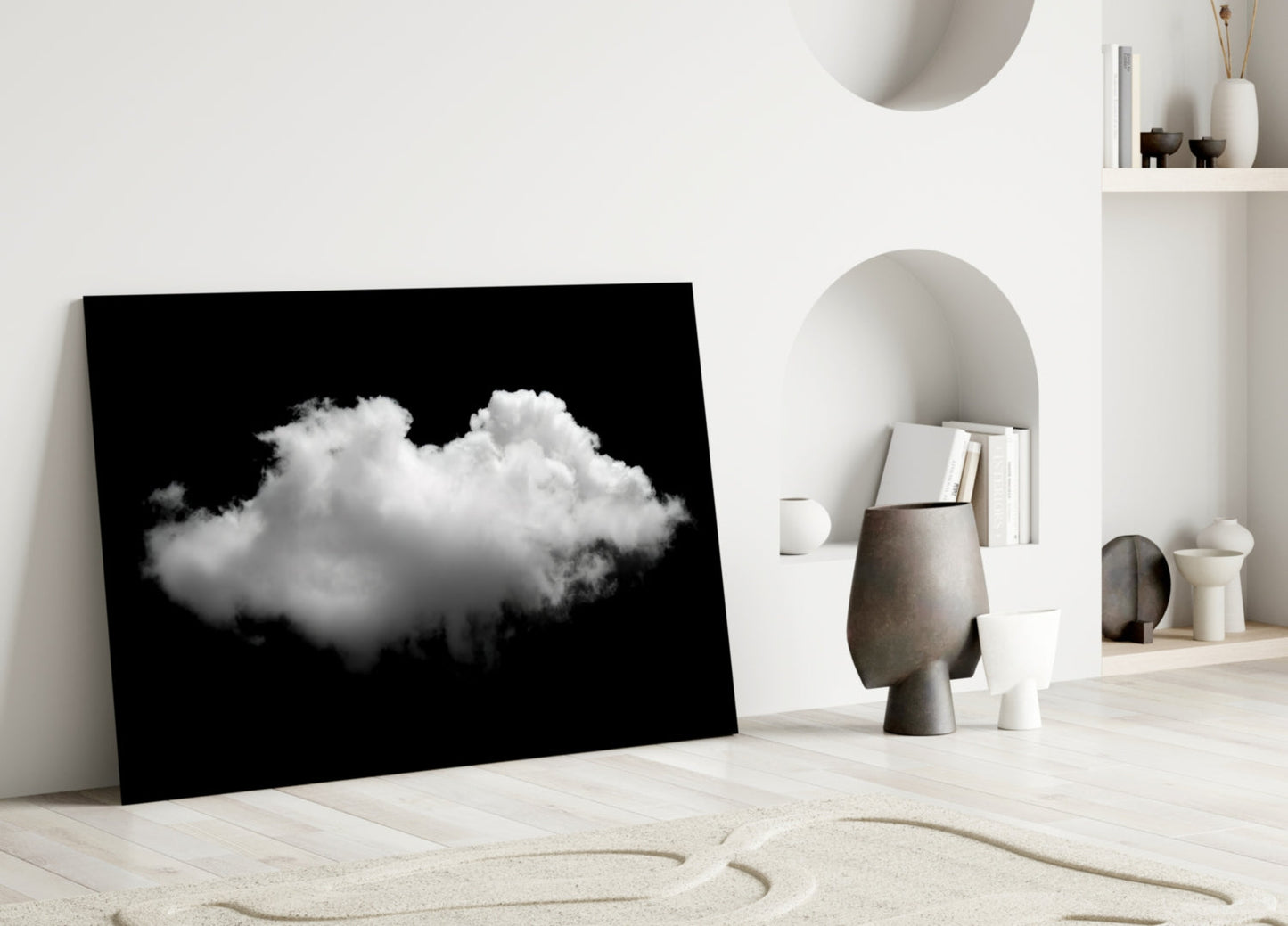 Black framed glass art displaying a white cloud against dark background, leaning against white wall in minimalist interior setting.