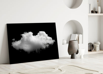 Black framed glass art displaying a white cloud against dark background, leaning against white wall in minimalist interior setting.