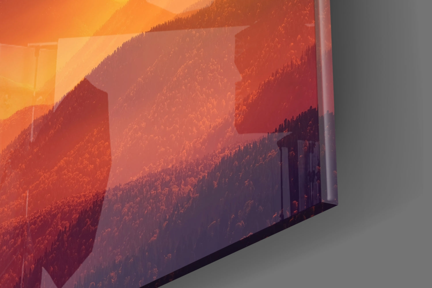 Angled view of glass wall art displaying warm-toned forested mountain landscape with orange and red sunset lighting.