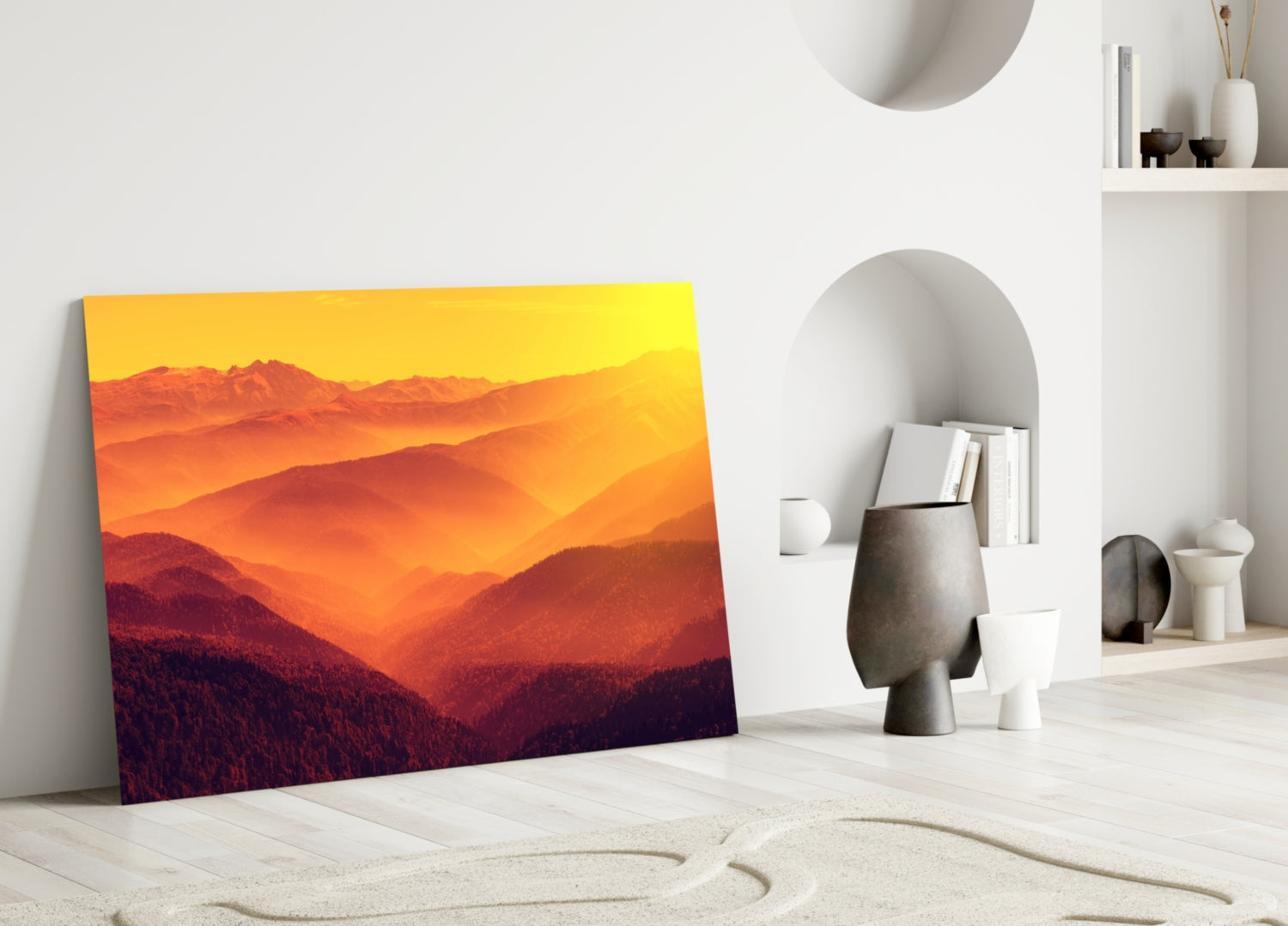 Glass wall art depicting layered mountains in warm sunset hues leaning against white wall in minimalist interior.
