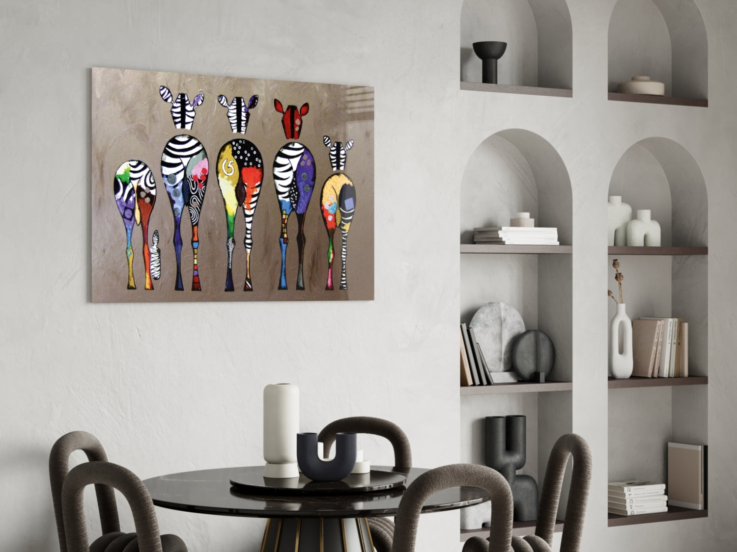 Colorful Zebras glass wall art displayed above a round black dining table with gray upholstered chairs in a modern interior with built-in shelving.